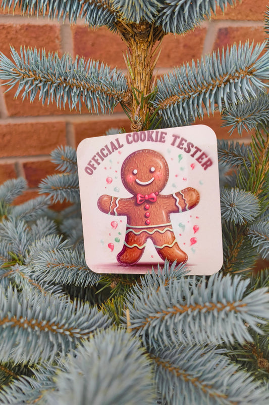 Square coaster with gingerbread man and “Official Cookie Tester” text displayed on a blue spruce tree.