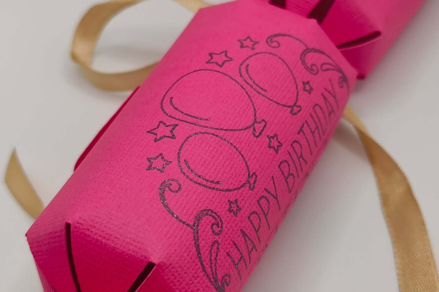 Personalised Birthday Crackers in bright pink with balloon design and golden ribbons for birthday celebrations.