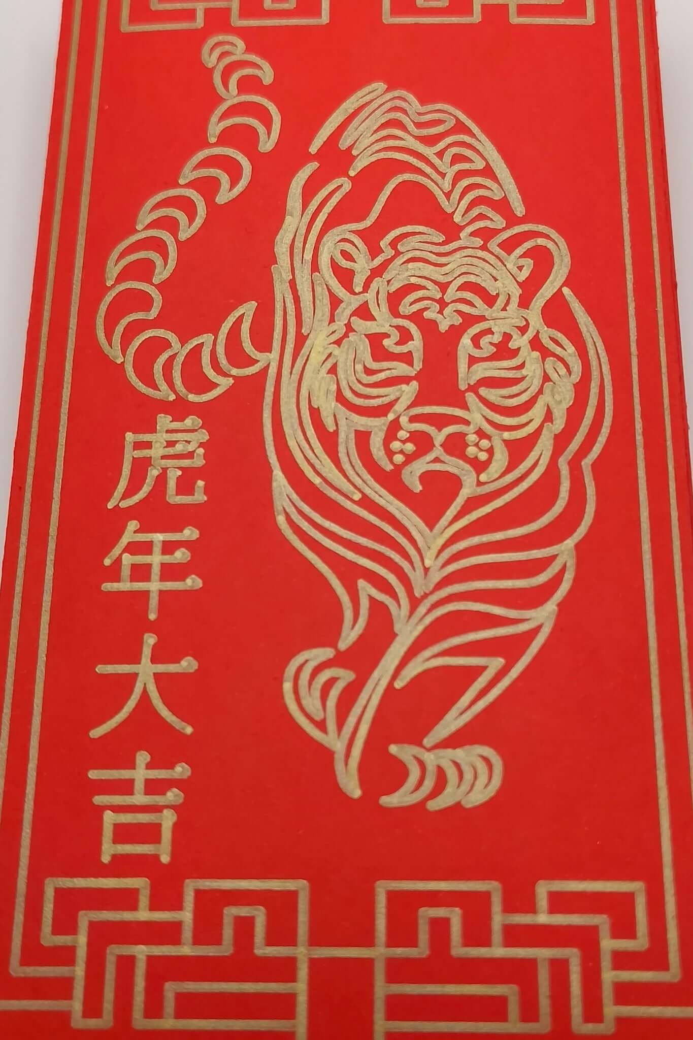Close-up of tiger illustration in gold pen on red Chinese New Year envelope.