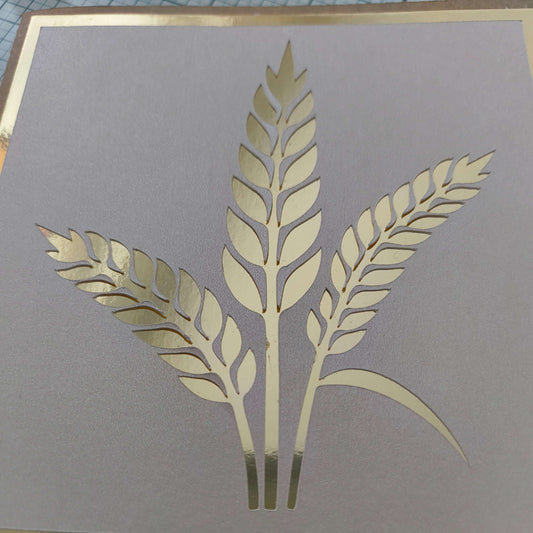 Close-up of a handmade card featuring a metallic gold wheat design on a light beige textured background, with a gold foil border.