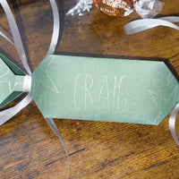 Close-up of green cracker featuring “Craig” with star doodles and silver ribbon ties, highlighting the textured cardstock design.