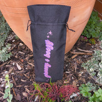 Black wine bag with sparkling pink “Groovy & Boozy” text shown upright outdoors among garden plants.