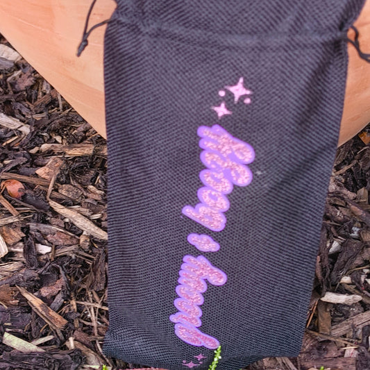 Black drawstring wine bag with pink glitter vinyl text “Groovy & Boozy” and stars, photographed outdoors against wood chip background.