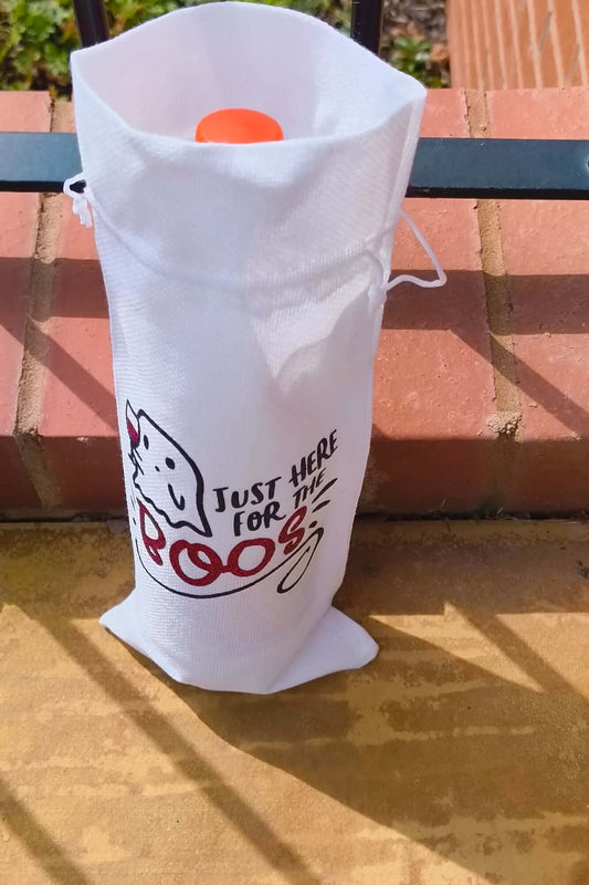 White Halloween wine bag holding a bottle with orange cap, ghost illustration and text "Just Here for the Boos", placed against brick steps.