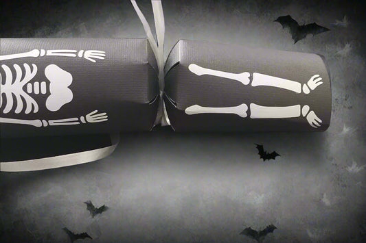 Halloween skeleton cracker with bones and ribcage design on black card, decorated with flying bat background.