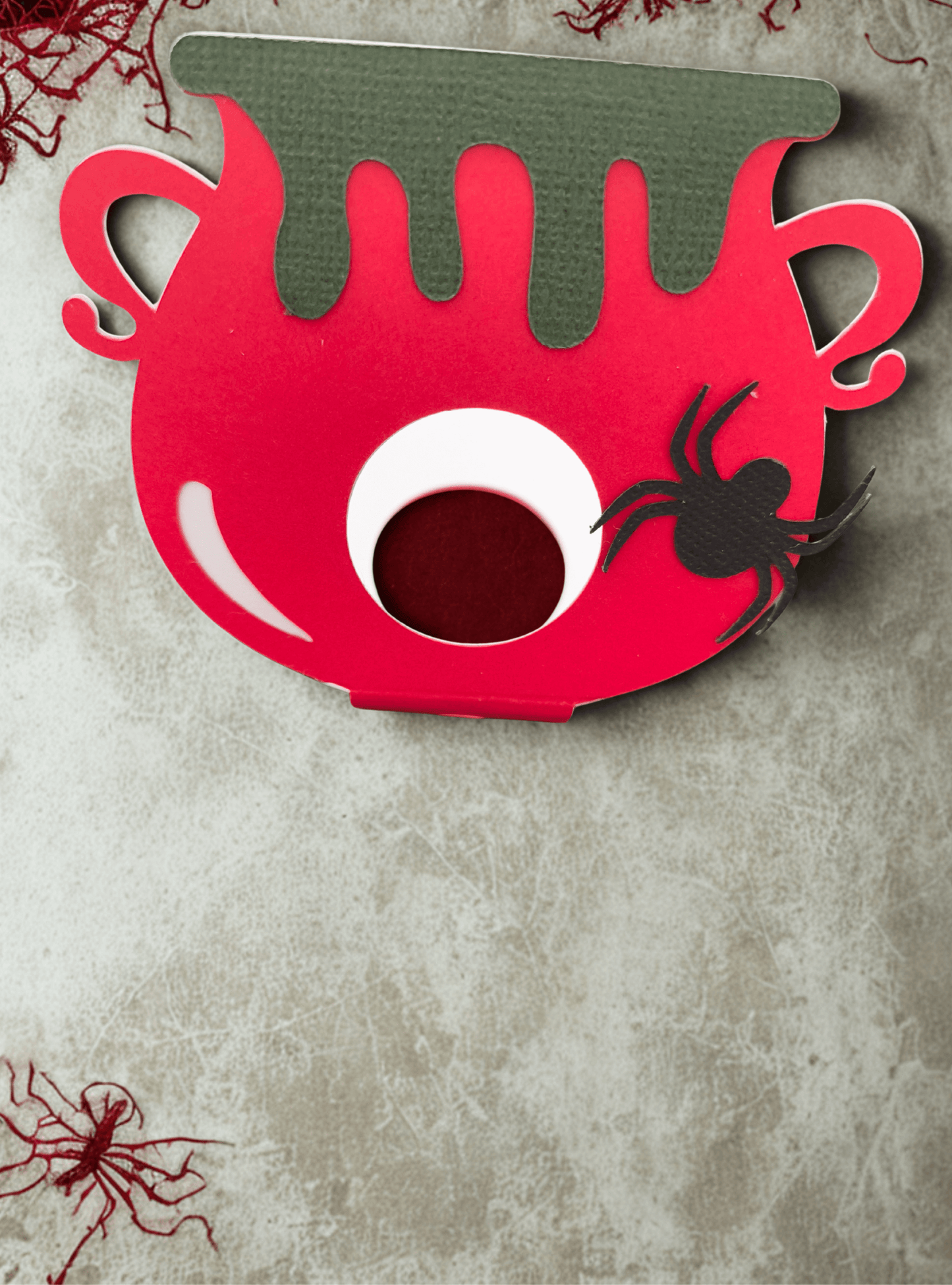 Colourful Halloween lollipop holder shaped like a cauldron, featuring a spider decoration and dripping green accents.