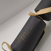 Angled view of handmade black cracker with gold ribbon bows and witch hat “Mum” text design