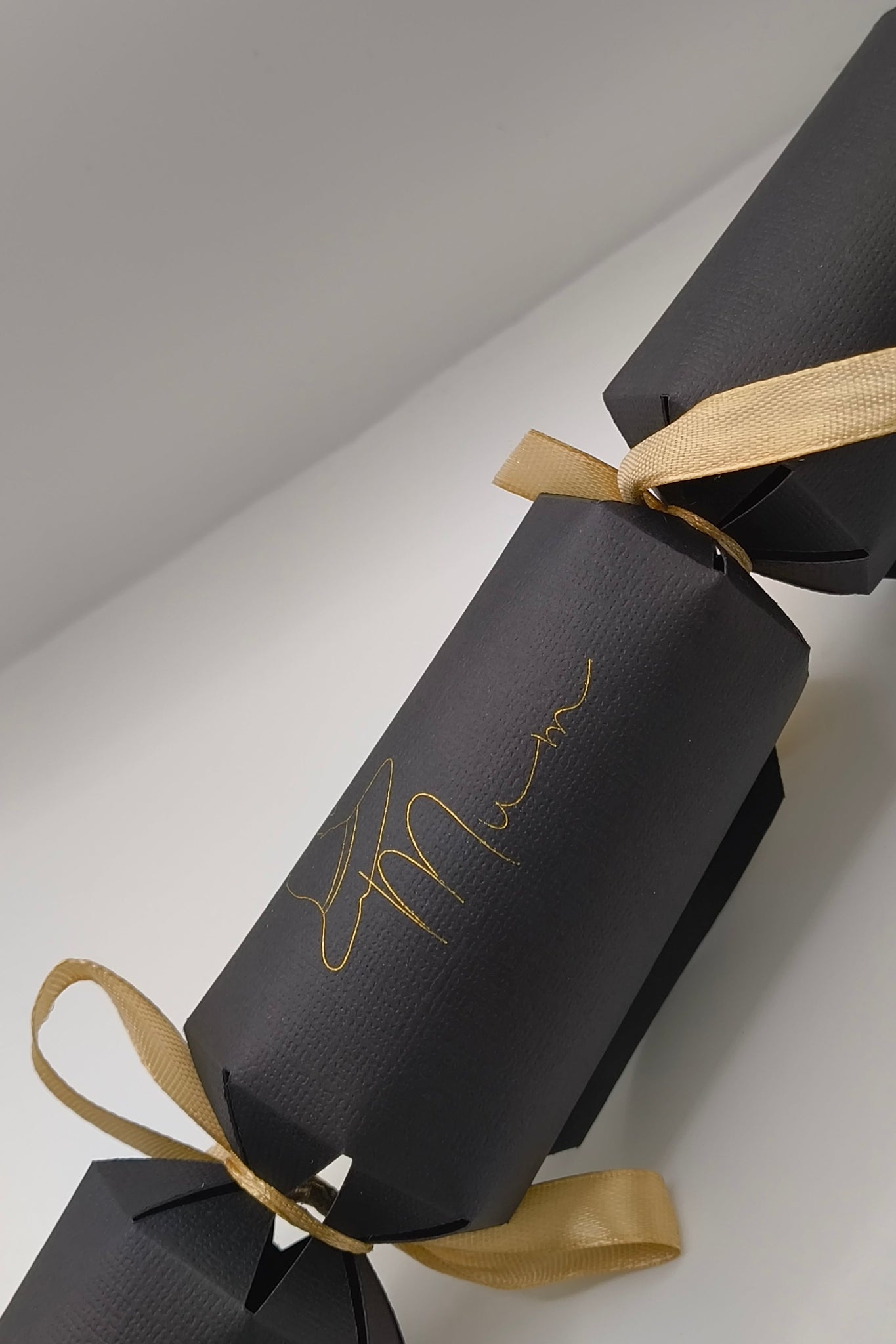 Angled view of handmade black cracker with gold ribbon bows and witch hat “Mum” text design