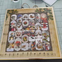 Handmade Christmas advent calendar decorated with vintage-style festive illustrations, including robins, owls, Santa Claus, wreaths, and winter animals, displayed on a craft mat with glue and scissors nearby.
