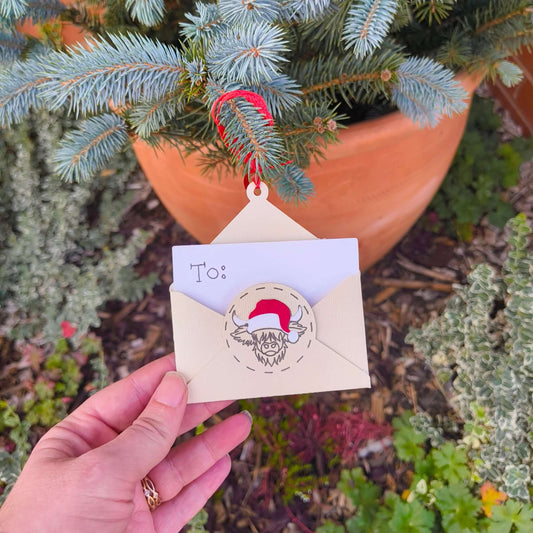 Handmade Christmas gift card envelope ornament held by hand against outdoor greenery