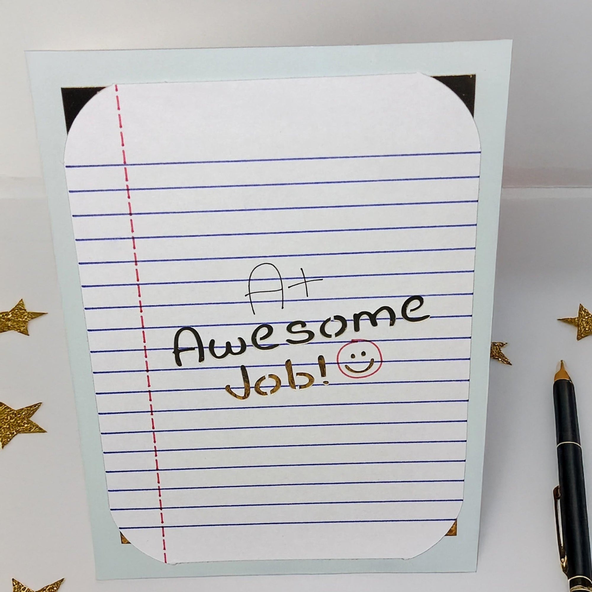 Handmade encouragement greeting card with A+ Awesome Job message, photographed from a top-down angle with gold star confetti and pen for school or student celebration keywords.