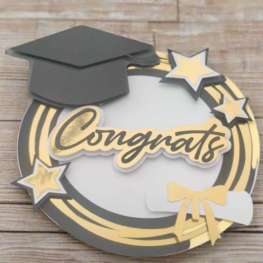 Handmade graduation card featuring a black mortarboard, gold “Congrats” text, gold stars, and diploma motif on a circular gold and white layered base. Ideal for graduation cards, scrapbook pages, and handmade gifts.