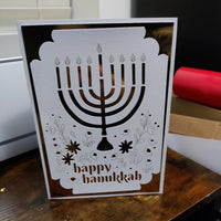 Handmade Happy Hanukkah greeting card featuring a cut-out menorah design with gold foil background and floral accents.