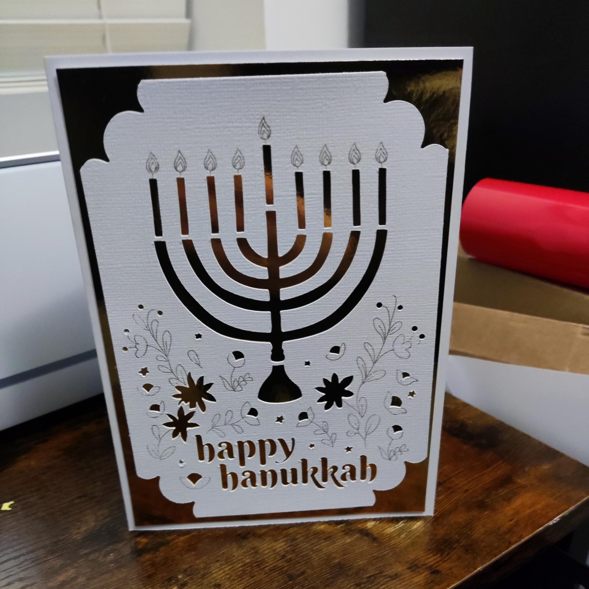 Handmade Happy Hanukkah greeting card featuring a cut-out menorah design with gold foil background and floral accents.