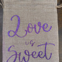 Handmade hessian bag with a natural woven texture and bold purple glitter script reading “Love is Sweet.” Sturdy and reusable with a simple drawstring fastening.