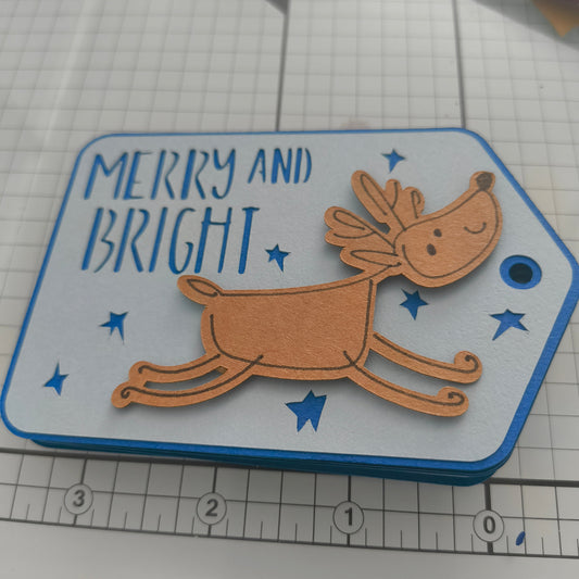 Handmade reindeer Christmas gift tag with “Merry and Bright” message, layered cardstock design on cutting mat