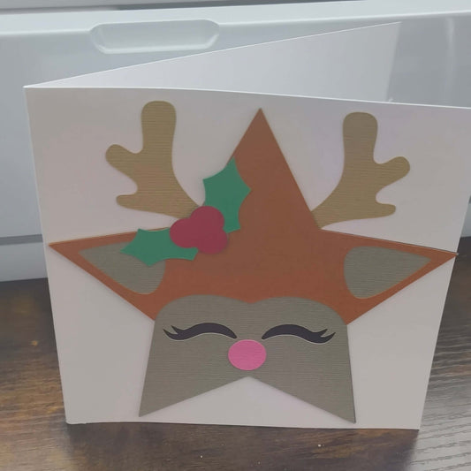 Handmade Christmas card featuring a reindeer with antlers, holly, and a pink nose on a star-shaped design.