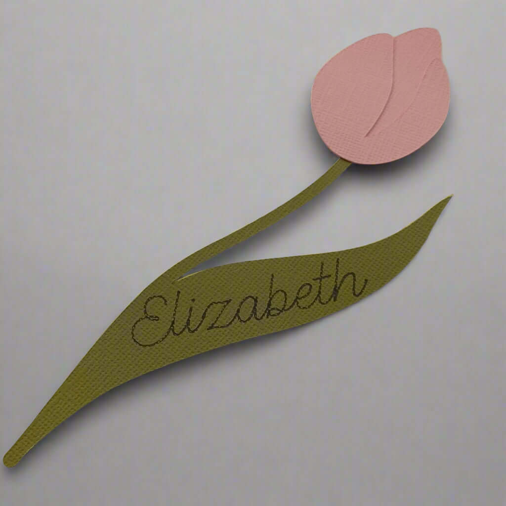 Handmade tulip-shaped place card in pink and green cardstock with the name “Elizabeth” on the leaf, laid flat on a plain background.
