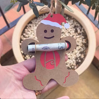 Gingerbread ornament hanging from a tree branch, featuring red monogram letter A and Santa hat.