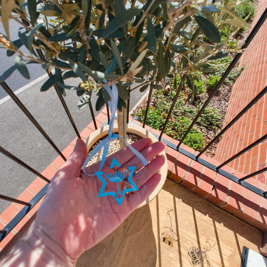 Person holding clear Hanukkah ornament with menorah and Star of David next to other acrylic decorations.