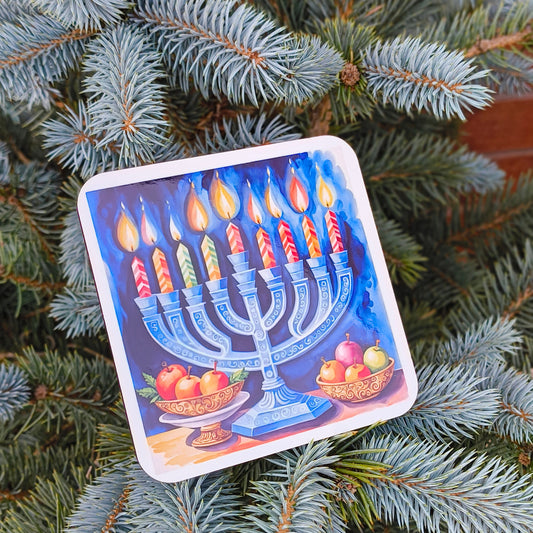 Hanukkah coaster with menorah and fruit bowls, placed on a potted blue spruce by a brick wall