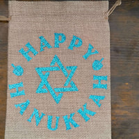 Flat lay of Hanukkah hessian gift bag with blue glitter Star of David and ‘Happy Hanukkah’ text