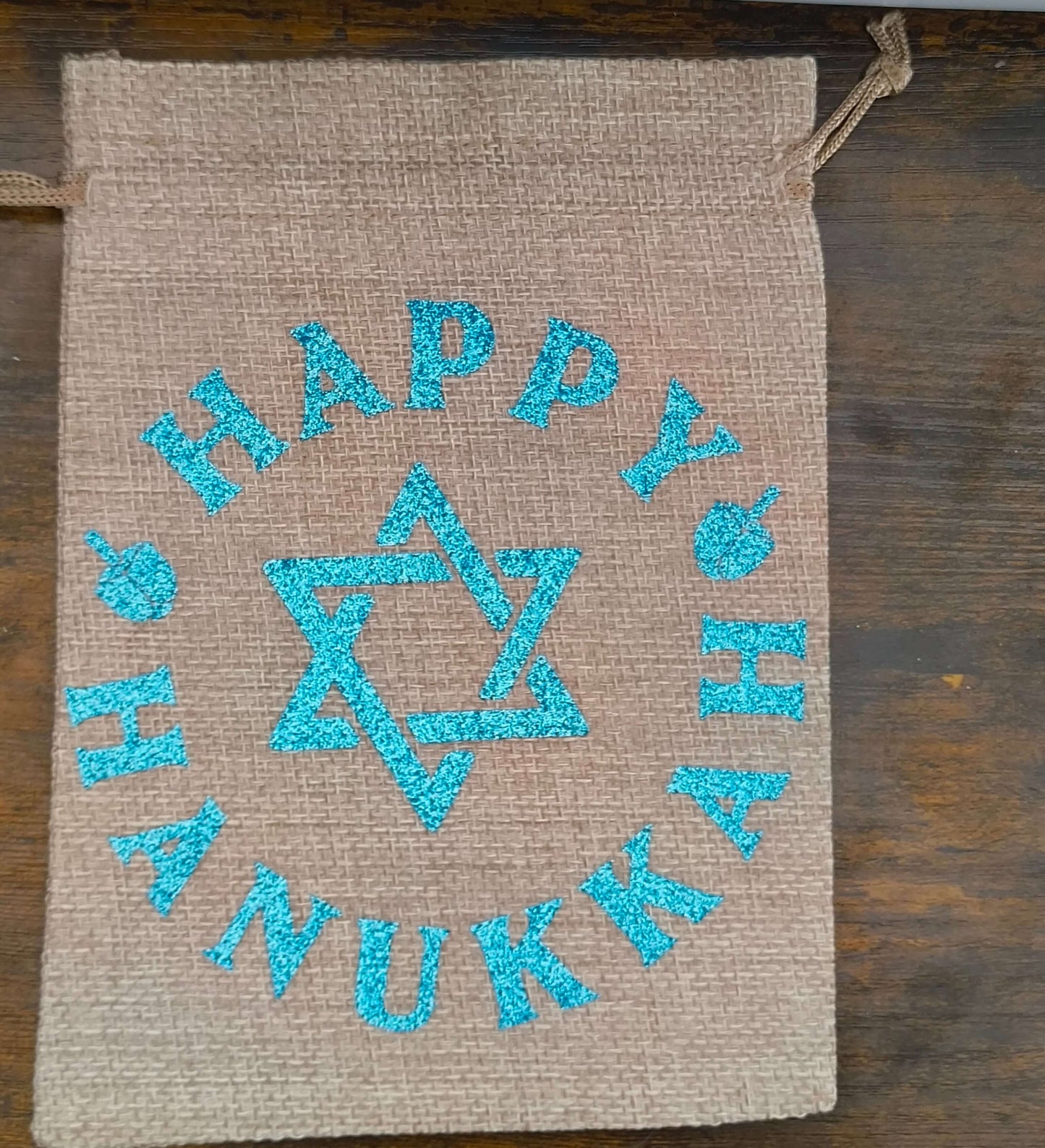 Flat lay of Hanukkah hessian gift bag with blue glitter Star of David and ‘Happy Hanukkah’ text
