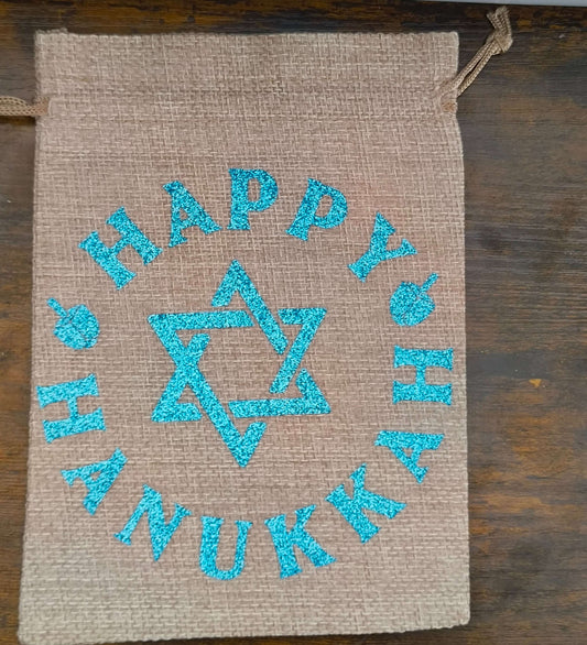 Flat lay of Hanukkah hessian gift bag with blue glitter Star of David and ‘Happy Hanukkah’ text