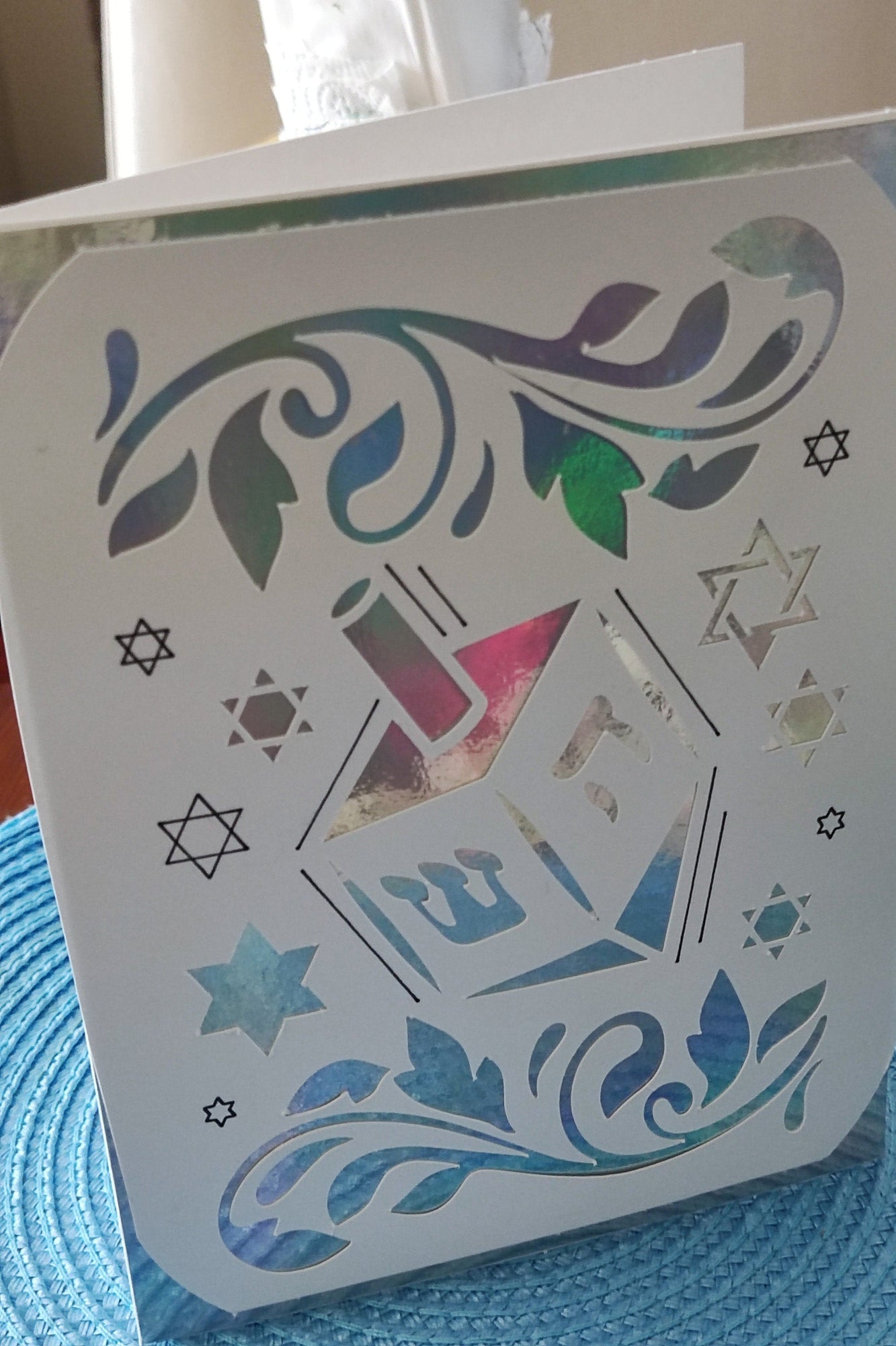 Hanukkah greeting card with dreidel cut-out and holographic silver-blue background on table