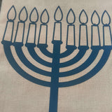 Close-up of a beige hessian gift bag with a blue vinyl Hanukkah menorah design, showcasing nine lit candles for the Jewish festival of lights.