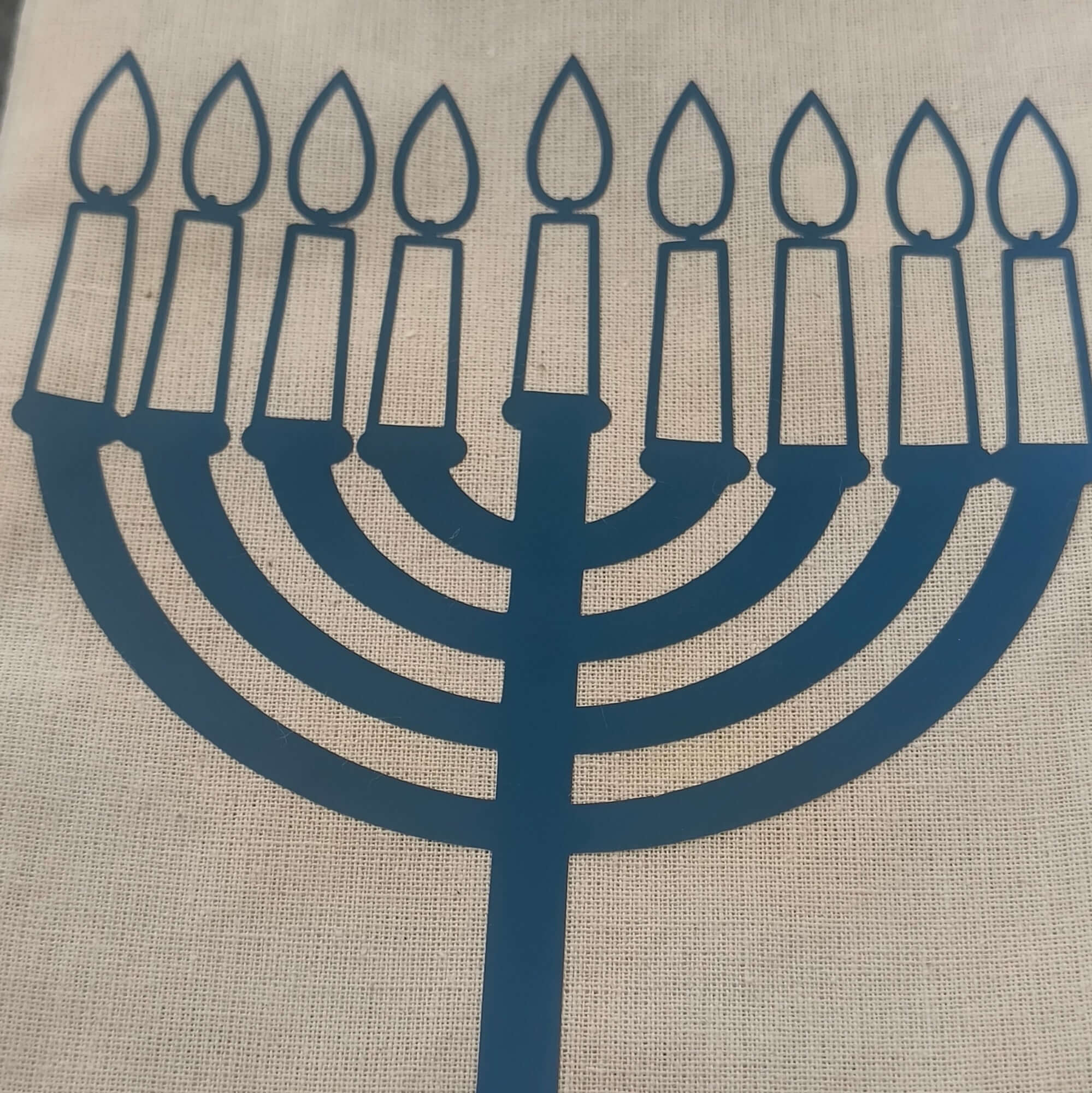 Close-up of a beige hessian gift bag with a blue vinyl Hanukkah menorah design, showcasing nine lit candles for the Jewish festival of lights.