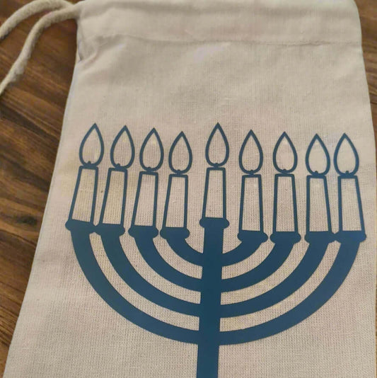 Natural hessian drawstring gift bag with a blue vinyl Hanukkah menorah design, placed on a rustic wooden background – perfect for festive gifting or party favours.