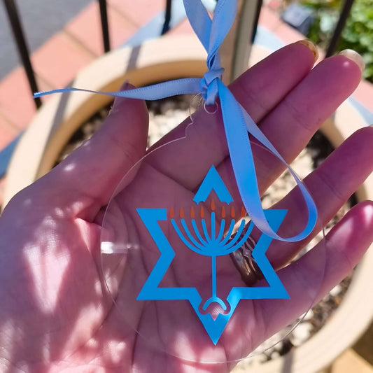 Clear Hanukkah tree ornament with blue ribbon, Star of David, and menorah design held in hand