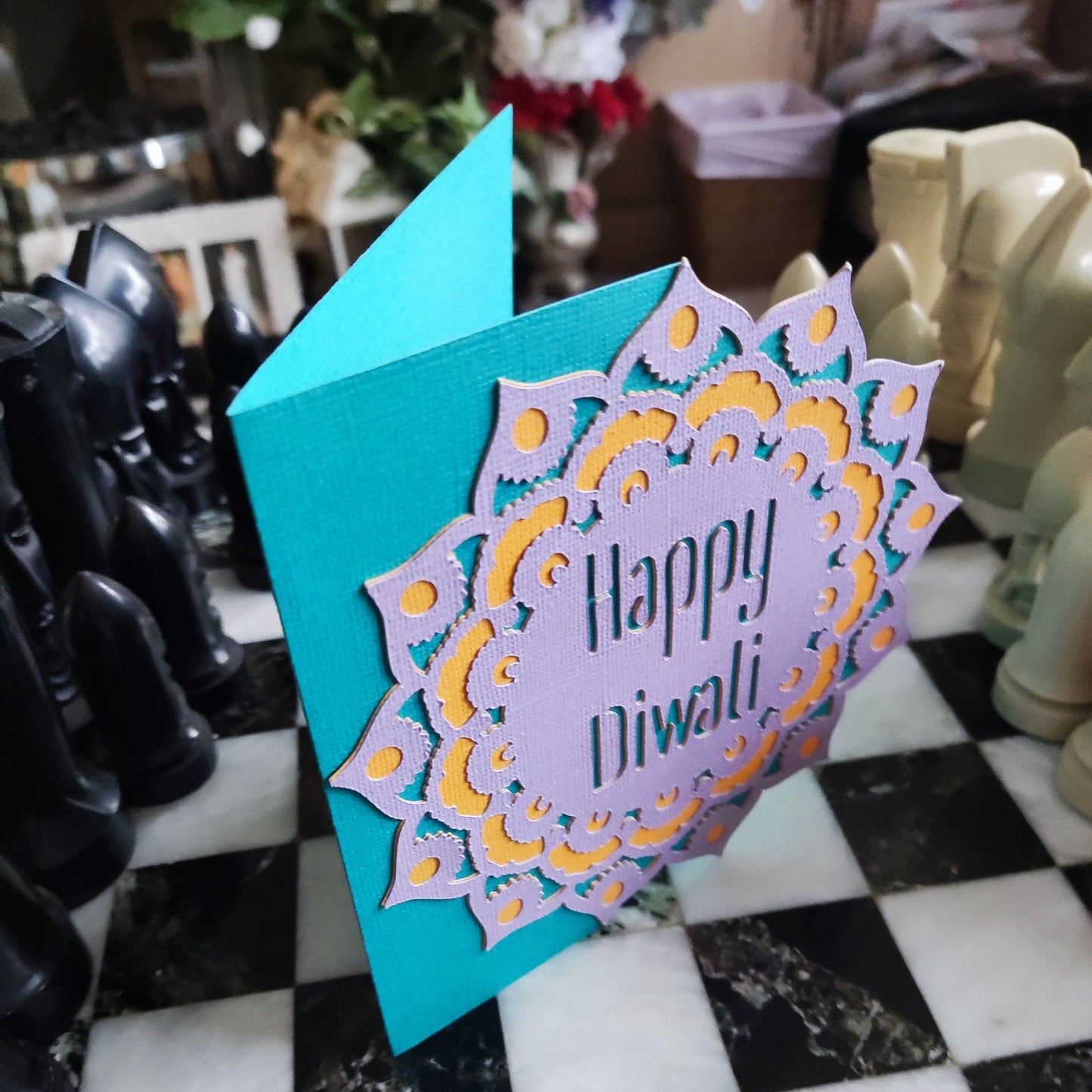 Handmade Diwali card with layered mandala design in purple, gold, and teal. Textured cardstock stands upright, showing bold festive colours.