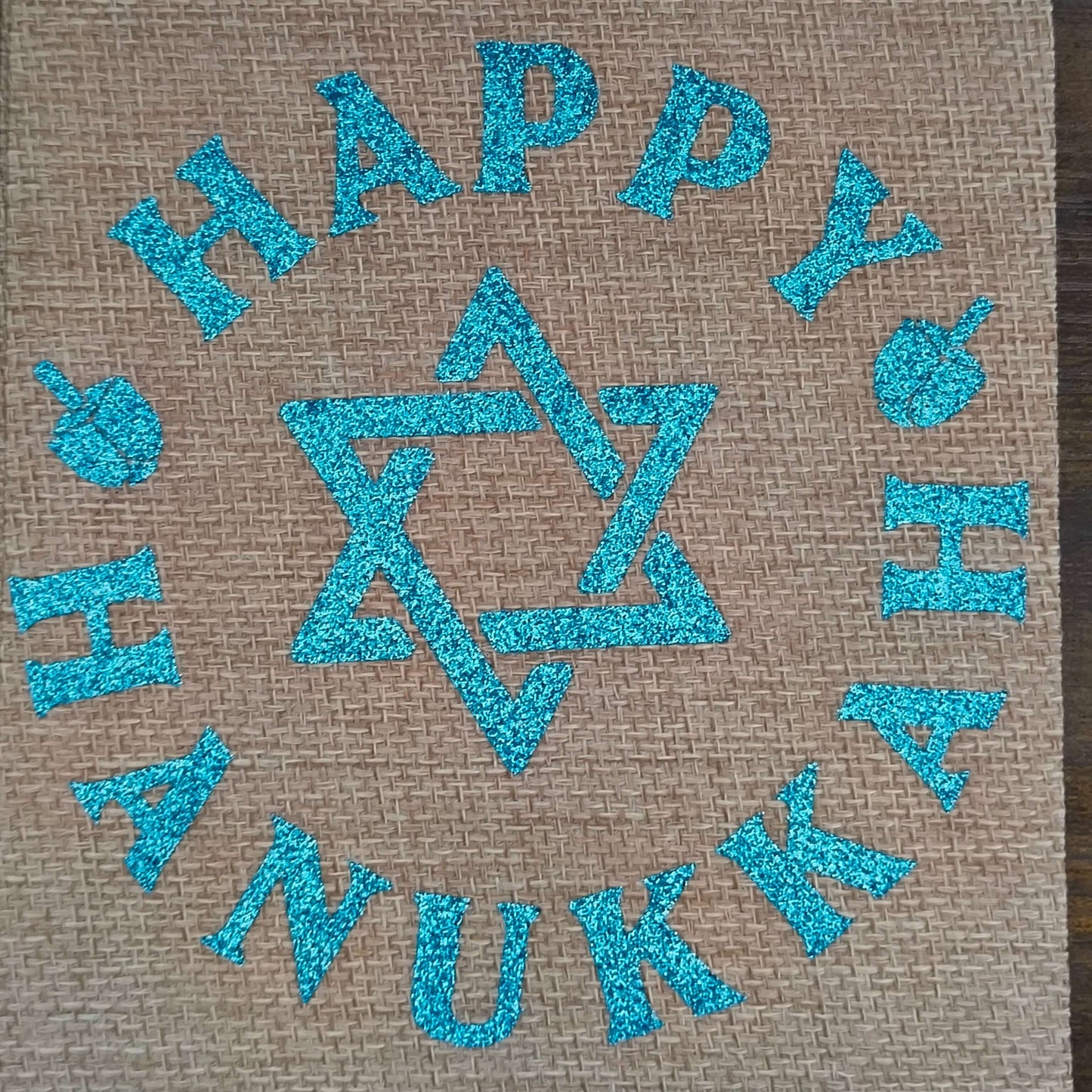Overhead photo of flat Happy Hanukkah hessian bag with blue glitter design and dreidels