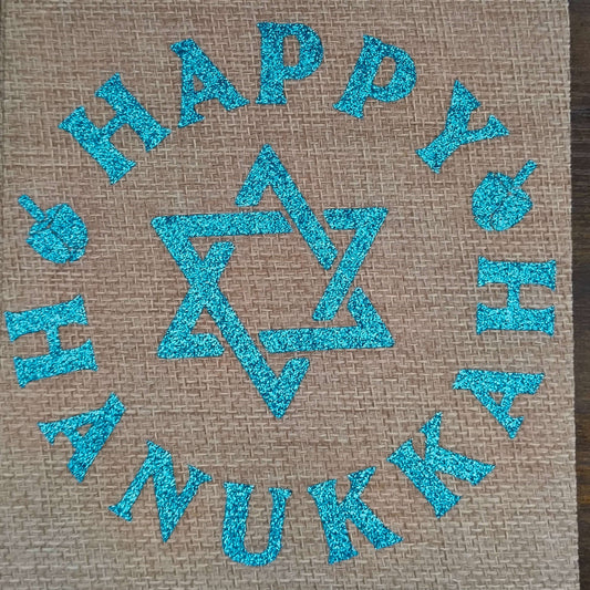 Overhead photo of flat Happy Hanukkah hessian bag with blue glitter design and dreidels