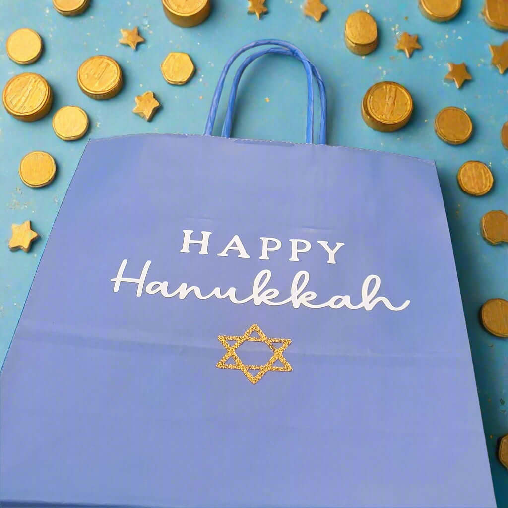 Blue Happy Hanukkah gift bag with white text and a gold glitter Star of David, surrounded by gold chocolate coins and festive stars on a blue background.