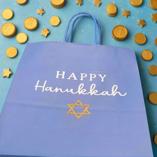 Blue Happy Hanukkah gift bag with white text and a gold glitter Star of David, surrounded by gold chocolate coins and festive stars on a blue background.