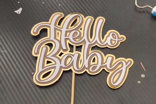 Gold layered cardstock 'Hello Baby' cake topper for baby showers or new baby celebrations.