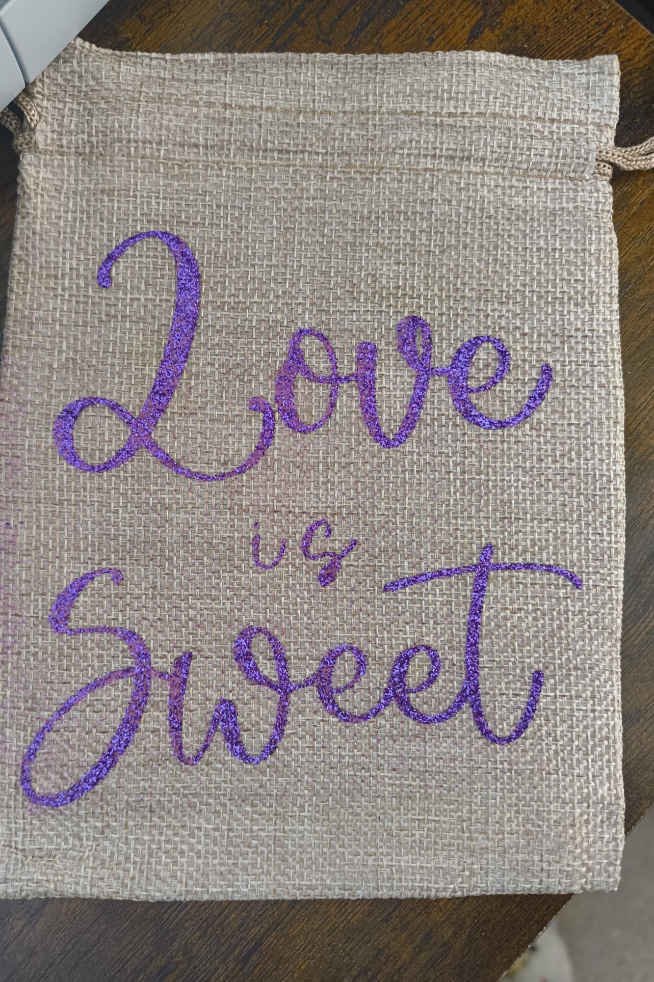 Rustic jute-style drawstring pouch featuring “Love is Sweet” in sparkling purple glitter. Compact size, ideal for sweets, favours, or small keepsakes.
