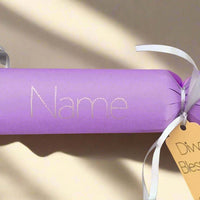 Handmade personalised Diwali cracker in lavender with white ribbon and gold tag reading 'Diwali Blessings', featuring custom name space in silver foil on a sunlit surface.