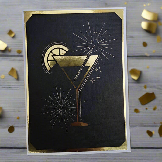 Luxury greeting card featuring gold foil cocktail glass, lemon slice, and fireworks on a black background with gold border.