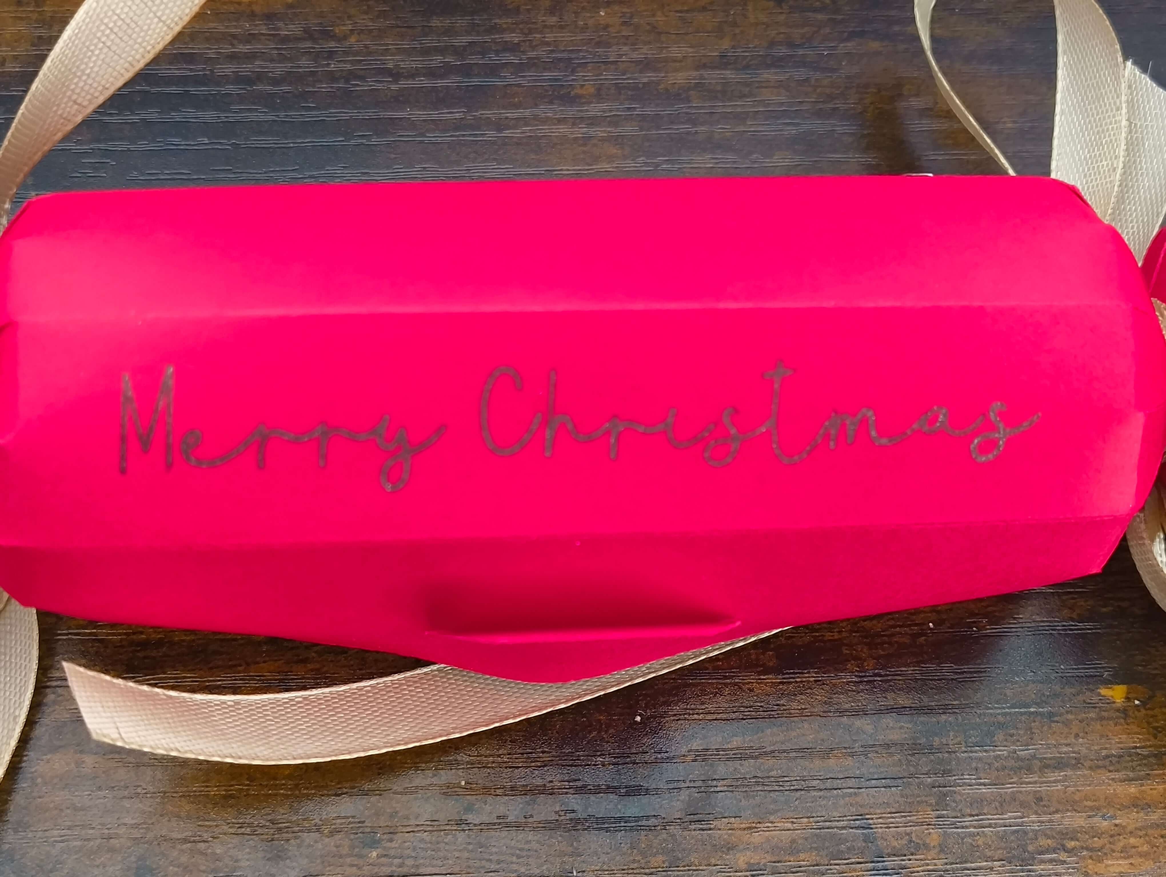 Personalised red Christmas cracker with glittery 'Merry Christmas' text and gold ribbon.