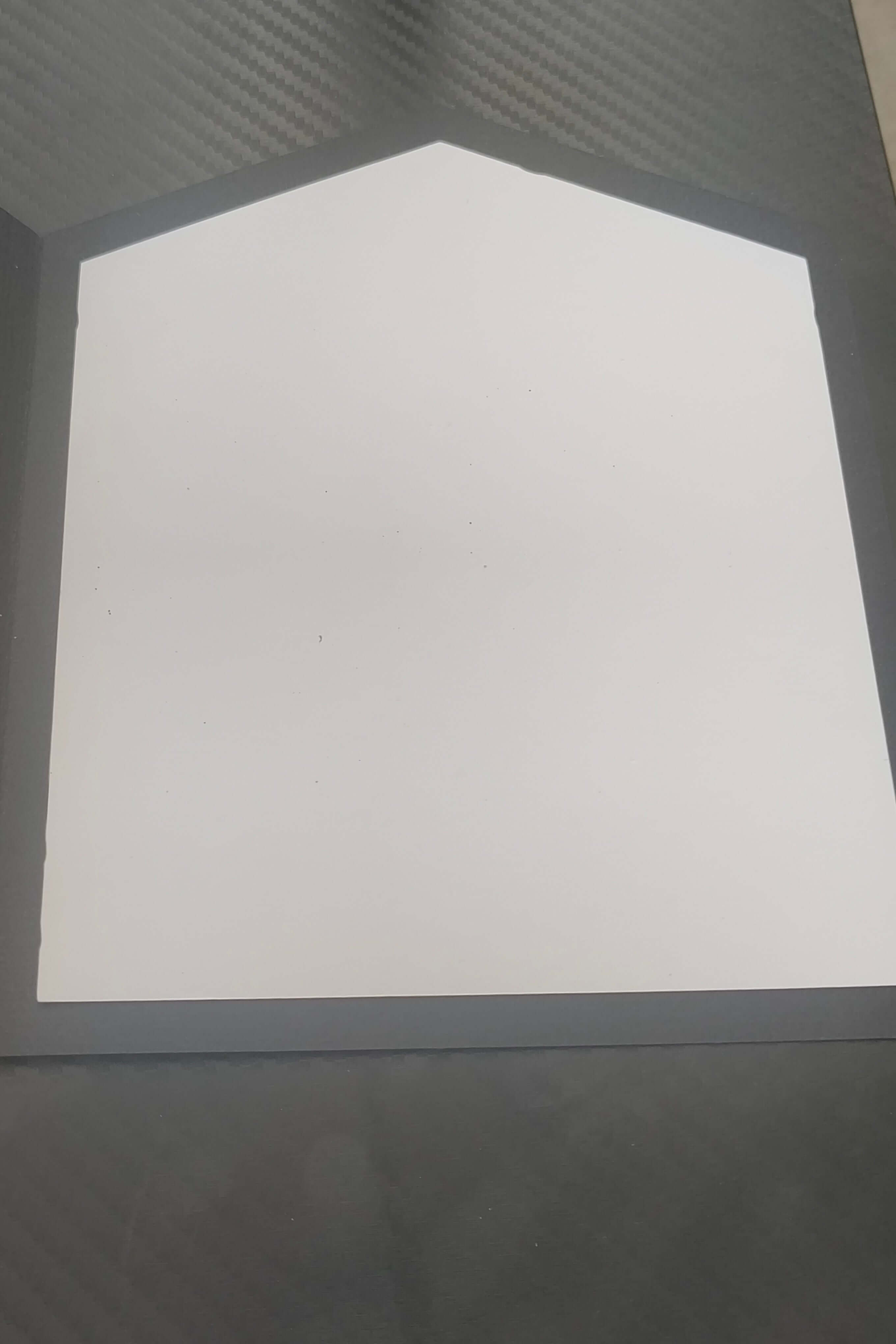 Blank folded card with a unique pentagon shape, placed on a textured black surface.