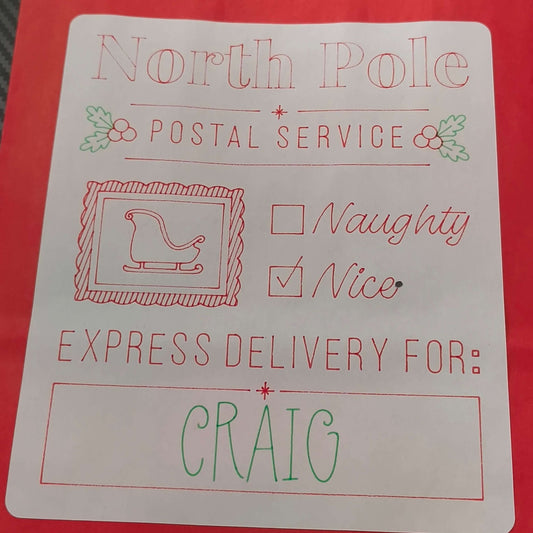 Red Christmas gift bag with a white label reading 'North Pole Postal Service'. The label includes holly decorations, a sleigh icon, checkboxes for 'Naughty' and 'Nice' with 'Nice' checked, and a message that says 'Express Delivery For: CRAIG' in festive red and green lettering.