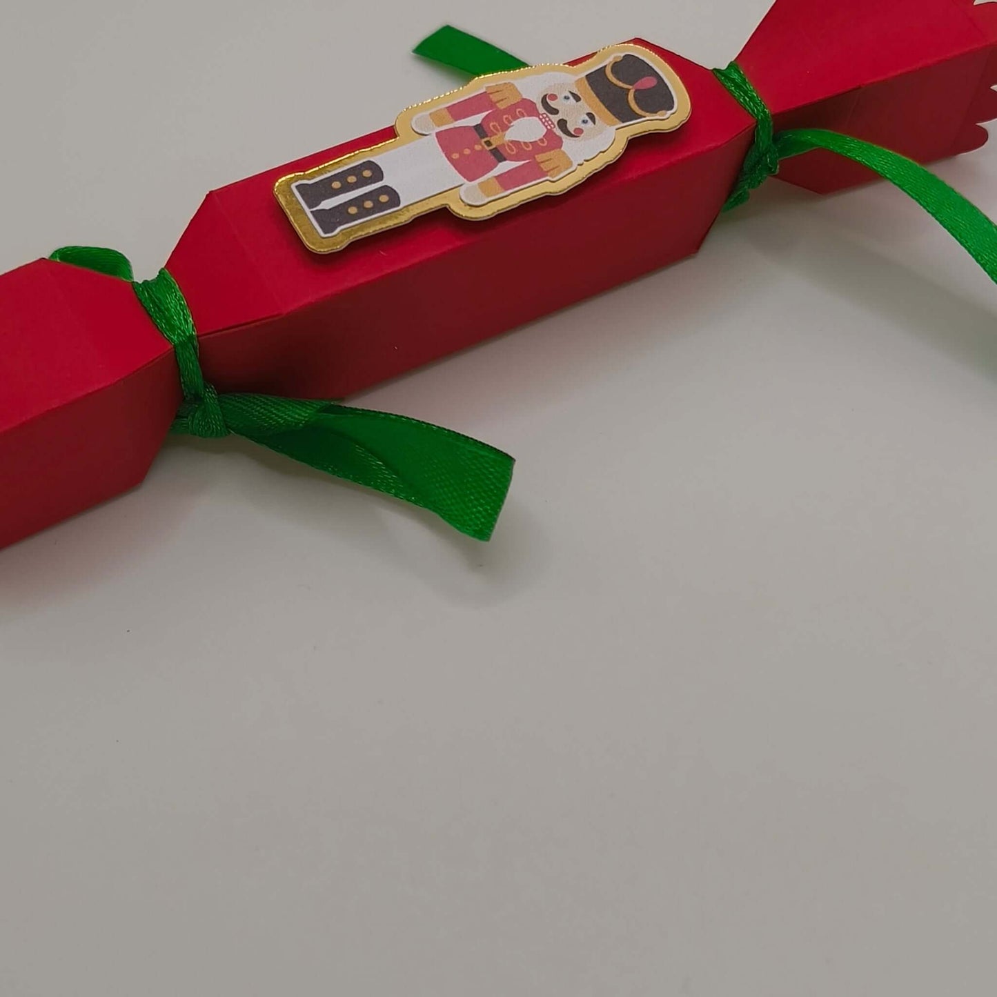 Festive cracker photographed from a lower angle, showing its neat construction and traditional red-and-green Christmas colour scheme.