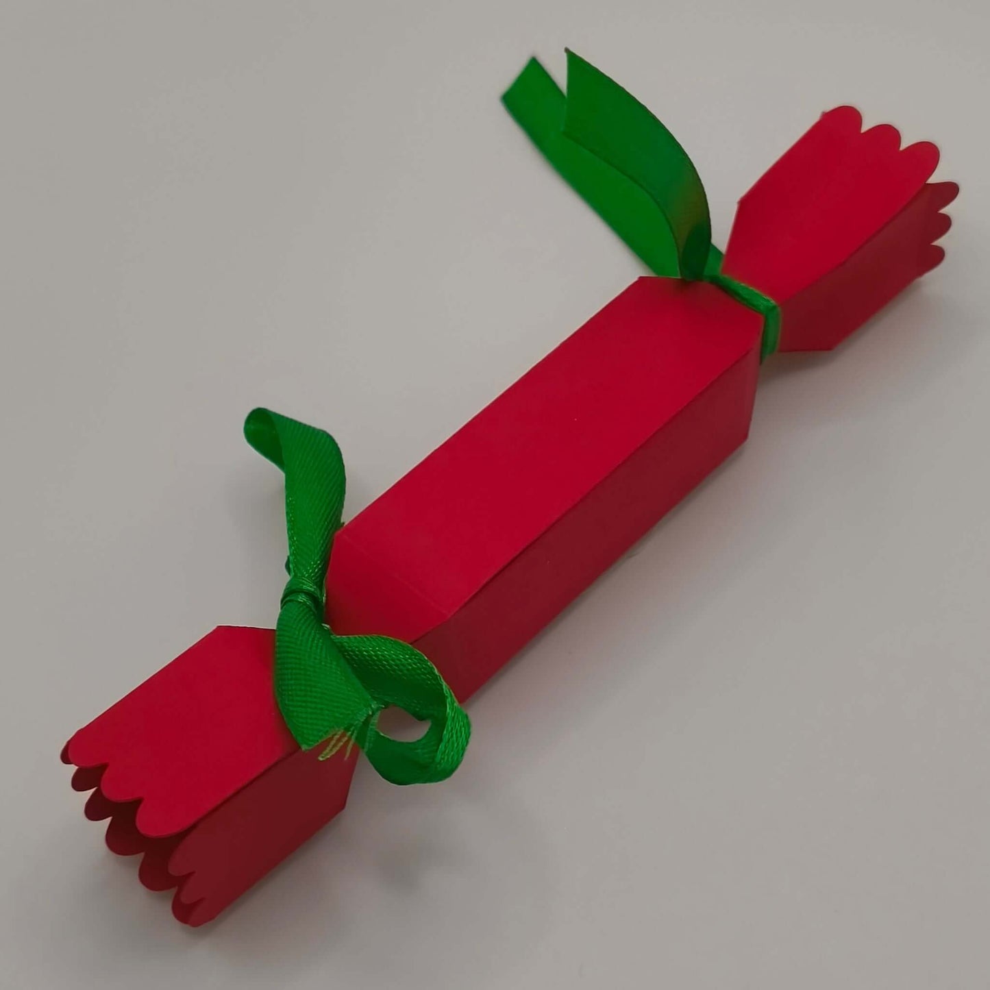 Reverse view of the cracker, tied at both ends with green ribbon. Shows clean folds, scalloped edging, and sturdy handmade finish.