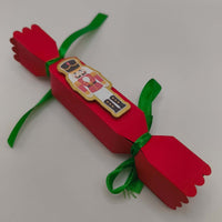 Handmade red Christmas cracker with green ribbon and nutcracker decoration. Festive and vibrant, sized for table settings or small gifts.