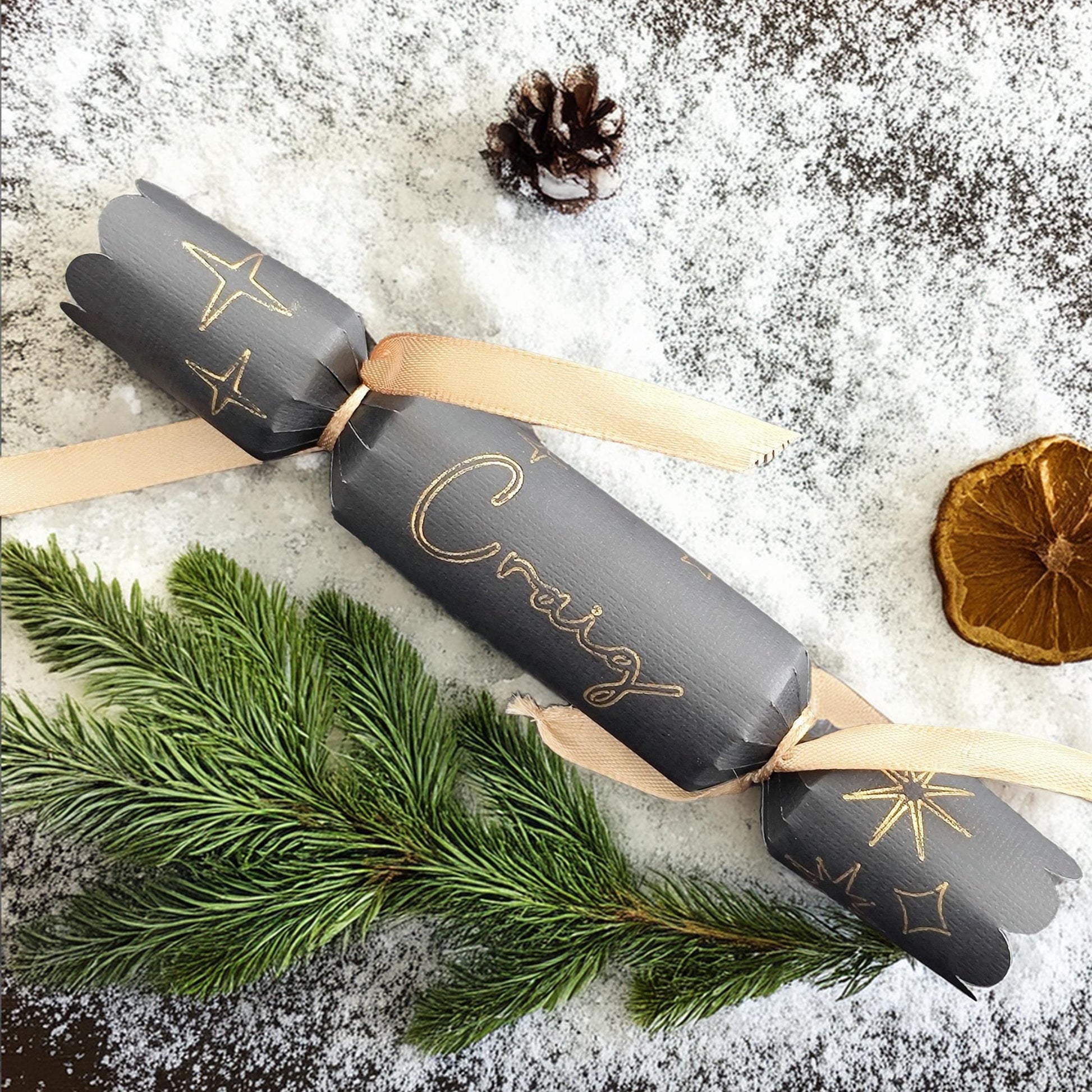 Black and gold personalised Christmas cracker with satin ribbon on snowy festive background