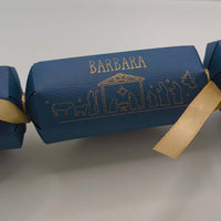 Handmade Christmas cracker in deep navy with gold Nativity design and personalised name, tied with golden satin ribbon.